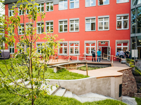 Der Innenhof der GLS Bank, man sieht ein paar Menschen auf der Terrasse, den Garten und einen Baum.