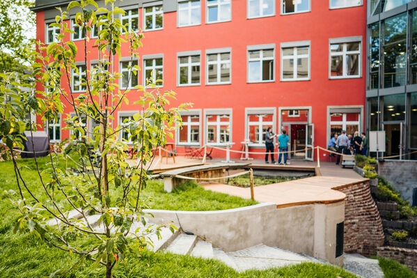 Der Innenhof der GLS Bank, man sieht ein paar Menschen auf der Terrasse, den Garten und einen Baum.