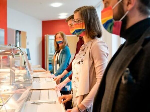 gls-bank-2022-nachhaltigkeitsbericht-wirkung-gesundheit Mitarbeitende der GLS Bank in stehen in der Kantine an. Sie tragen einen Mundschutz.