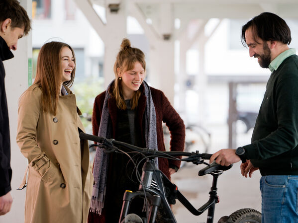 Eine Gruppe Menschen steht um ein Fahrrad herum und lachen gemeinsam.