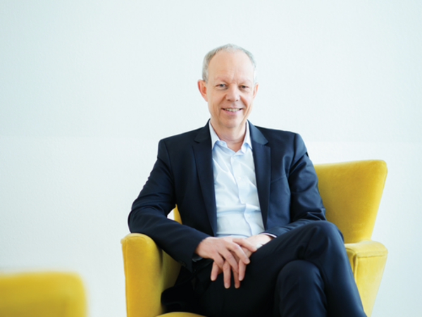 gls-bank-nachhaltigkeitsbericht-2022-thomas-jorberg-vorstand Der ehemalige GLS Bank Vorstandsvorsitzende Thomas Jorberg sitzt auf einem gelben Sessel und lächelt in die Kamera