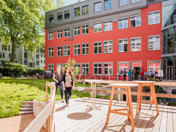 gls-bank-2022-nachhaltigkeitsbericht-wirkung-gesundheit-innenhof-garten Man sieht zwei Mitarbeitende, die durch den Innenhof und Garten der GLS Bank laufen.